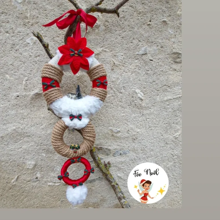 Couronne décorative en corde avec fleurs rouges et pompons blancs, suspendue à une branche.