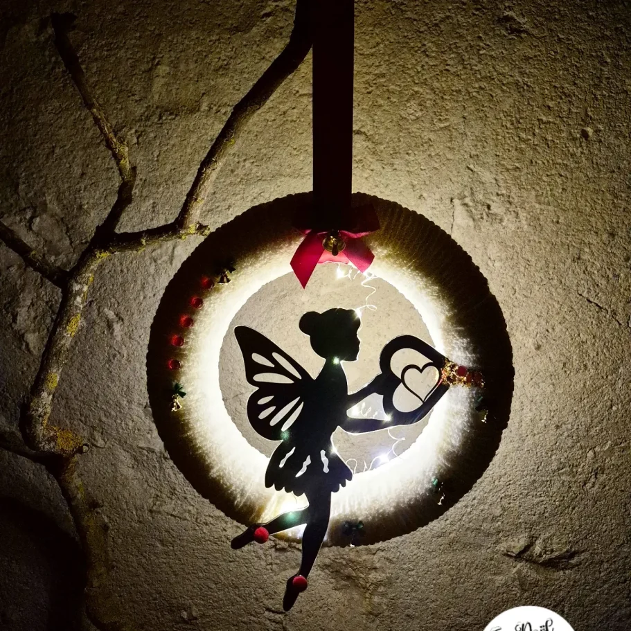 Fée silhouette décorative avec des ailes, suspendue dans un cadre lumineux.