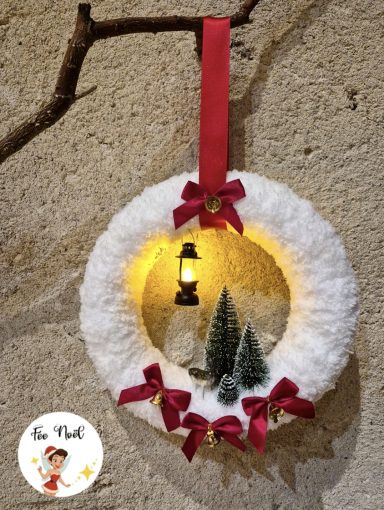 Couronne de Noël en feutre avec un lampion, des sapins et des nœuds rouges.